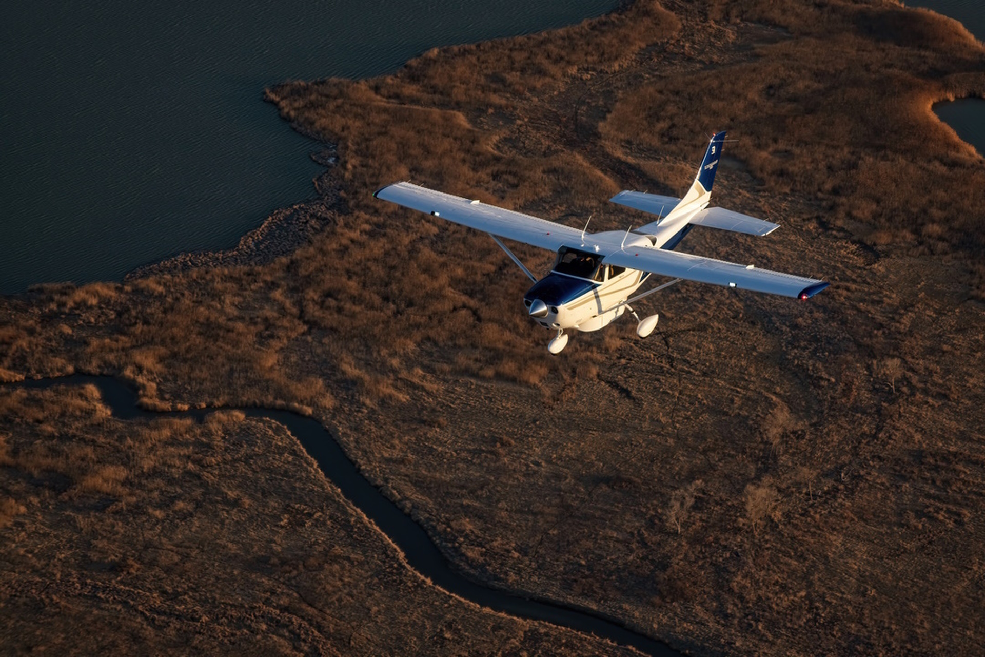 Single-engine aircraft in flight over wetlands at golden hour