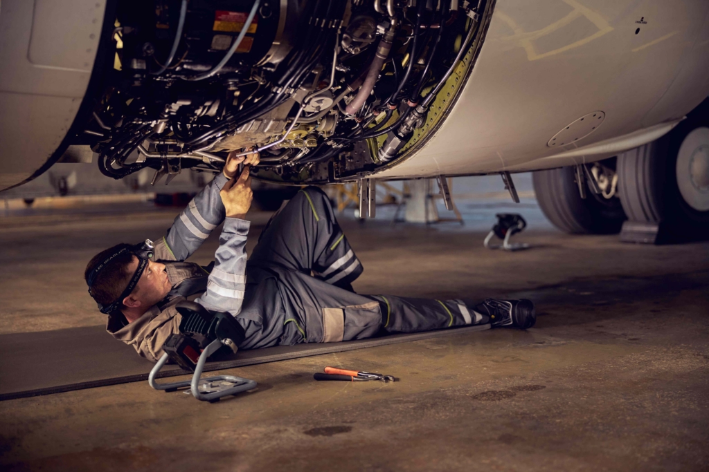 Technician performing maintenance underneath an aircraft engine